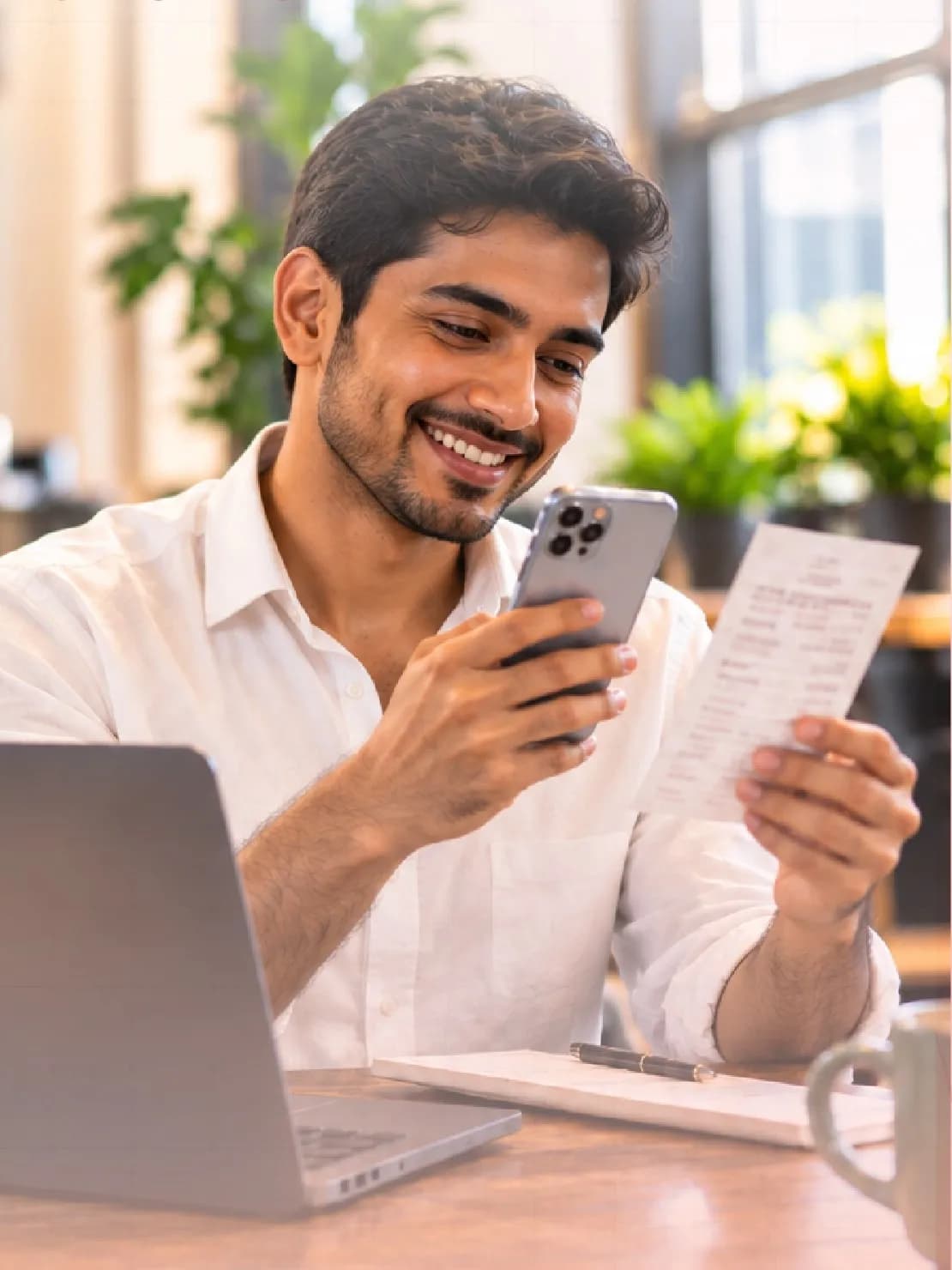 An employee at a café smiles at his phone while photographing a paper receipt
